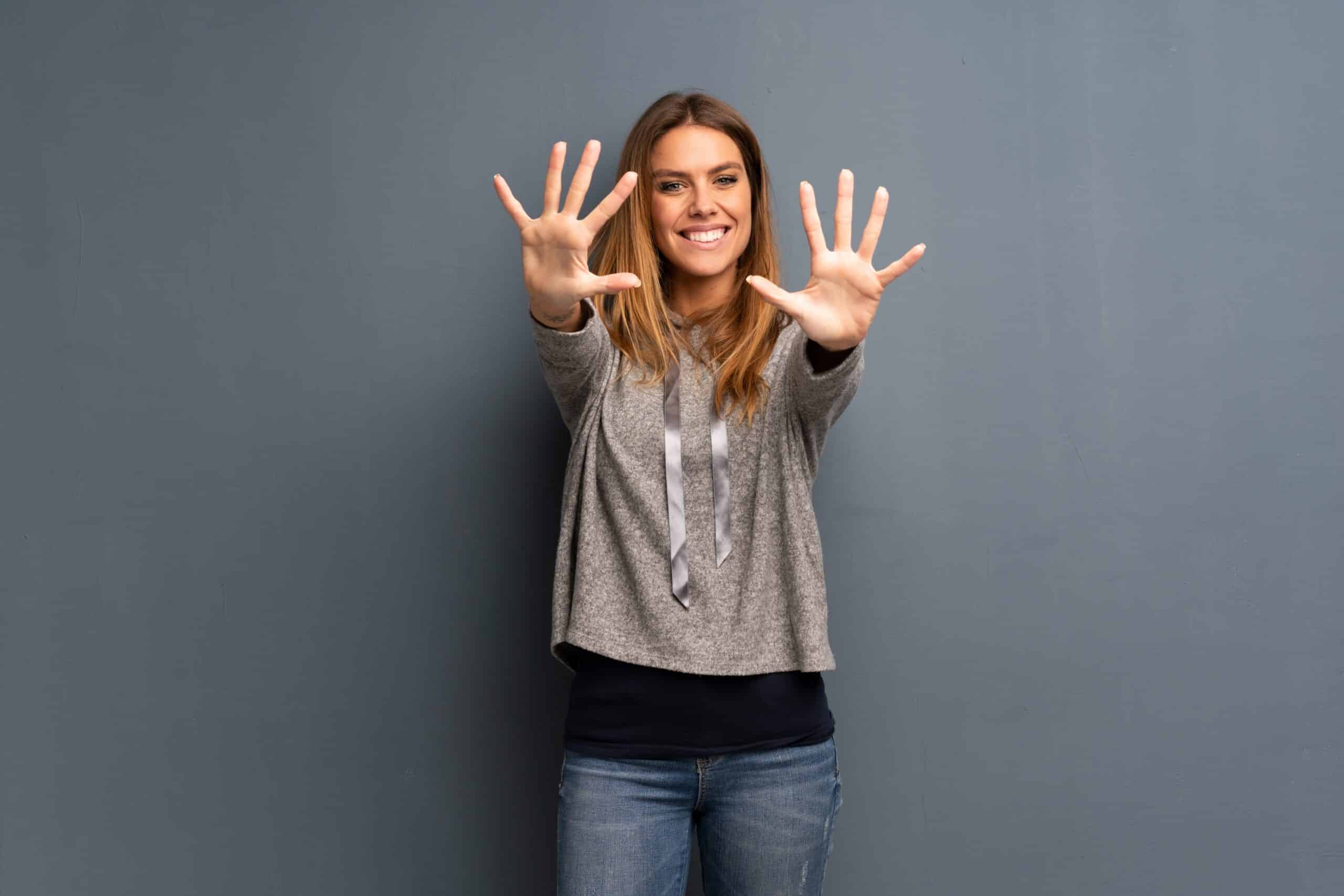 Blonde woman over grey background counting ten with fingers